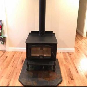 Black free-standing stove on stone matte on pine wood floors.