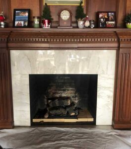 Fireplace with outdated logs, bricks, white marble surround and chestnut wood mantel before facelift - Mantel decorated with pictures and clock etc. - white marble surrounds the firebox - the mantel has dental molding.